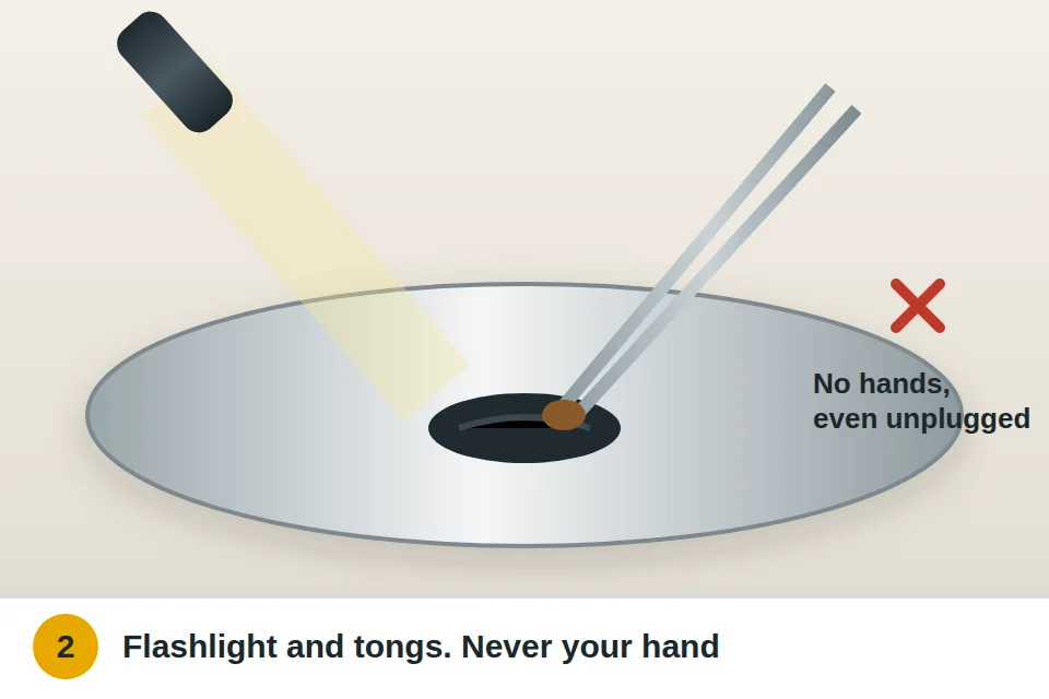 Flashlight shining down into a garbage disposal while tongs remove a fruit pit