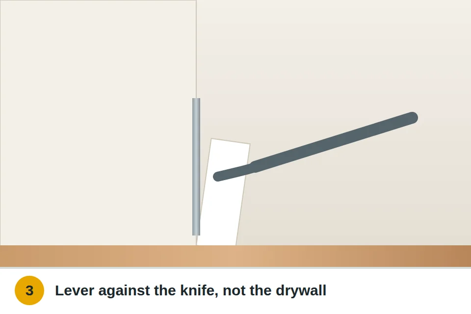Flat pry bar levering the baseboard off with a putty knife between it and the wall