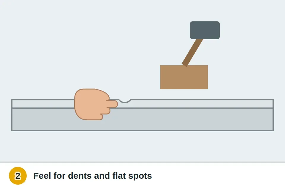 Finger running along the track rail to feel a small dent, with a wood block and hammer to ease it back