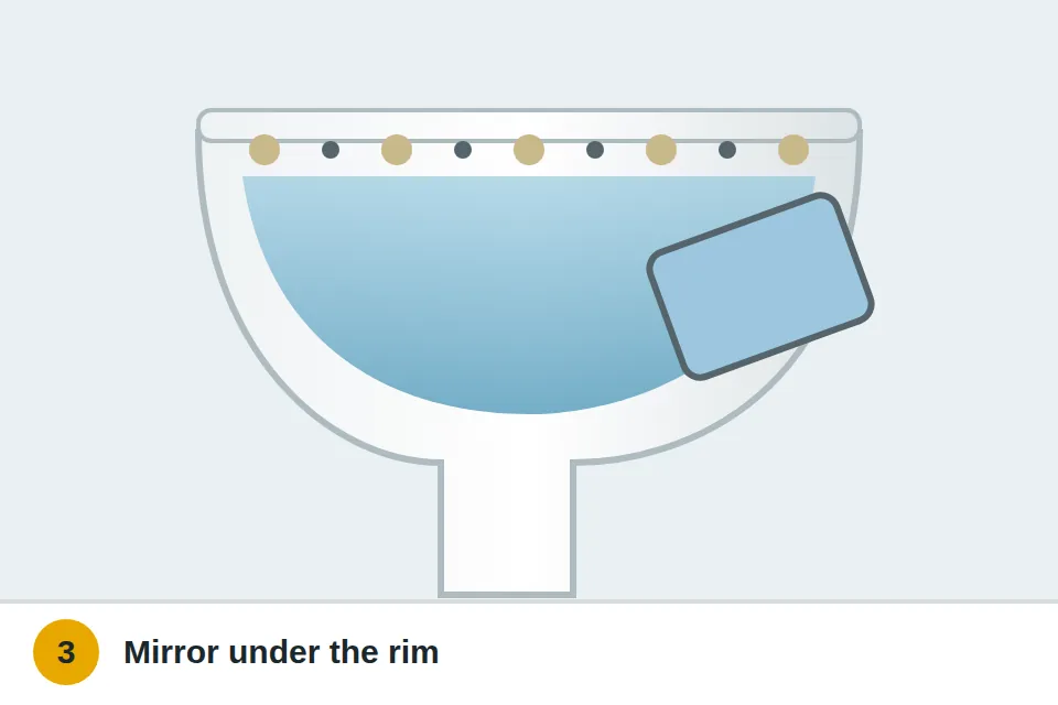 Small mirror held under the toilet bowl rim showing mineral crust around the rim holes